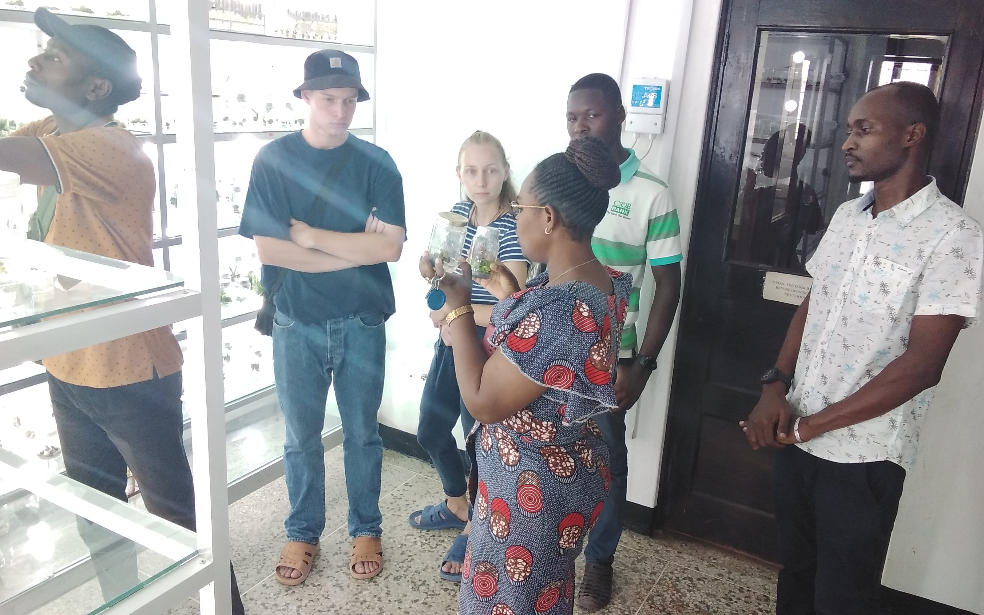 Dr. Happyness Mollel (carrying two bottles) researcher from TARI Mikocheni gives a brief to guests from Germany on how various crop planting materials such as pineapples and cassava can be produced using Tissue Culture Technology at TARI Mikocheni.